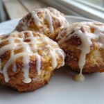 Close-up of three golden brown apple fritter treats drizzled heavily with white vanilla glaze.