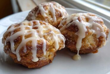 Close-up of three golden brown apple fritter treats drizzled heavily with white vanilla glaze.