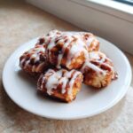 A close-up of several freshly baked cinnamon roll bites drizzled with white icing on a white plate.