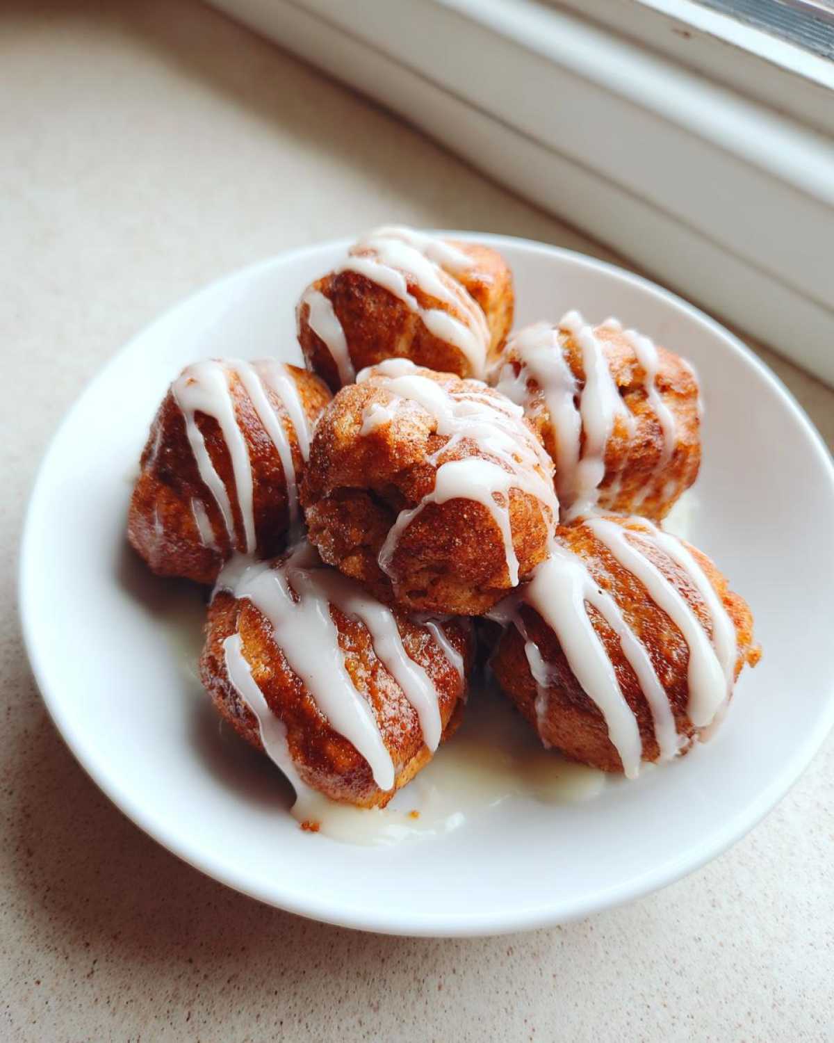 A small white plate holds six golden brown cinnamon roll bites drizzled generously with white vanilla icing.