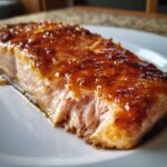 Close-up of a perfectly cooked, flaky salmon fillet topped with a thick, shiny orange-brown glaze.