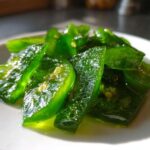 Close-up of glossy, bright green slices of candied jalapenos sitting in a light syrup on a white plate.
