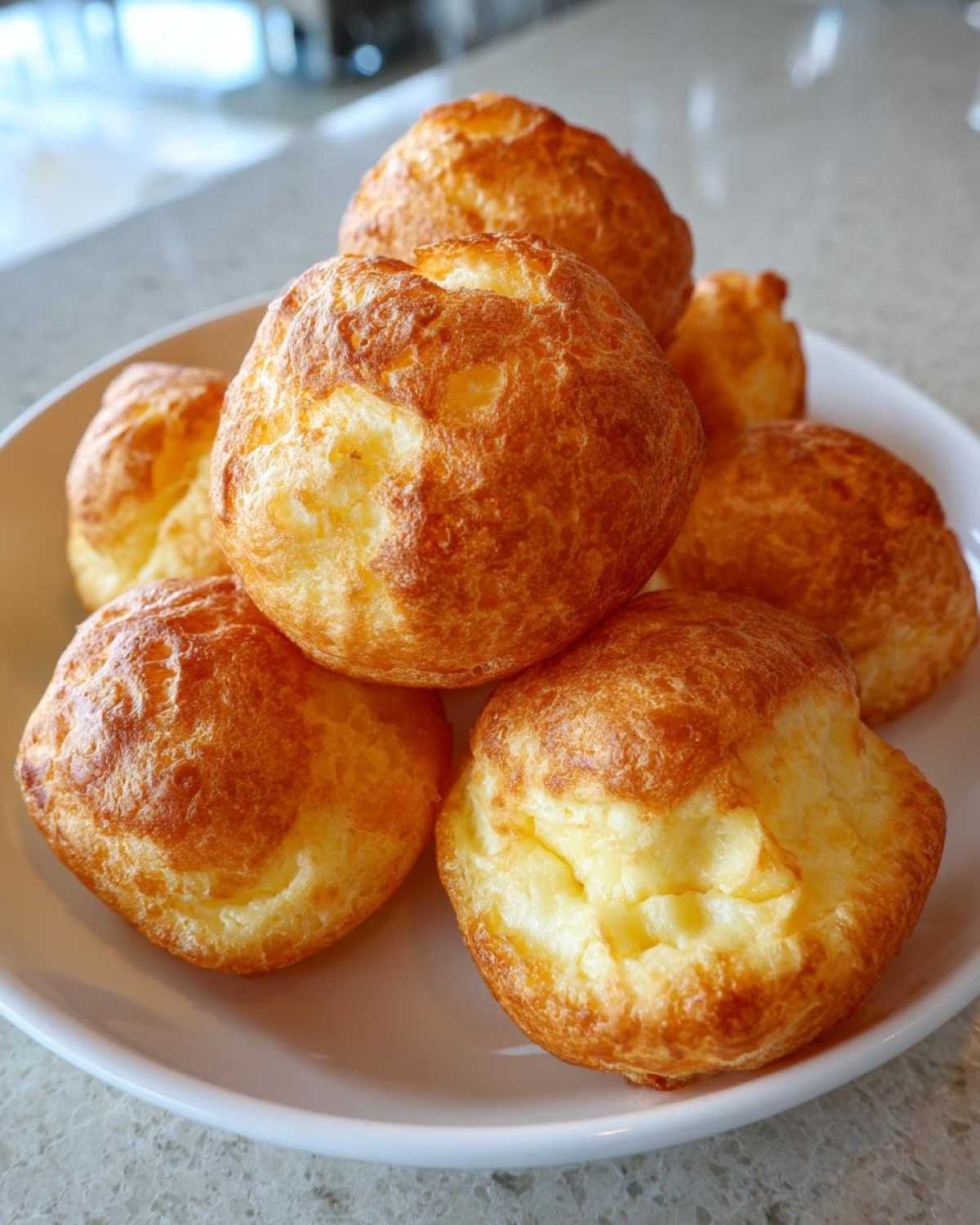A stack of freshly baked, golden brown brazilian cheese bread puffs piled high on a white plate.