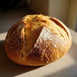 A perfectly baked, round loaf of Italian bread with a golden, crackled crust dusted lightly with flour.