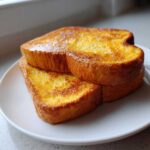 Two golden brown slices of easy french toast stacked slightly on a white plate.
