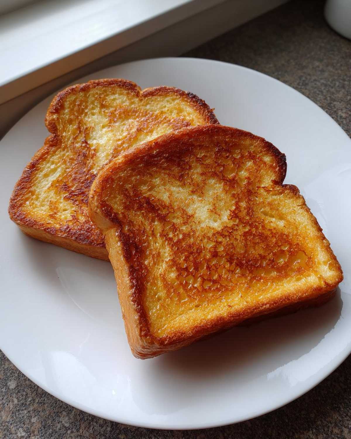 Two perfectly golden brown slices of easy french toast served on a white plate.