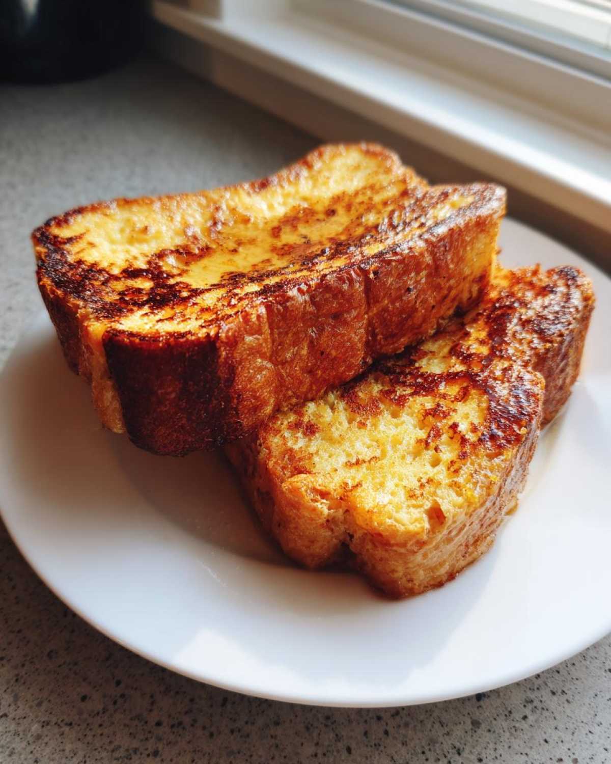 Two thick slices of golden brown, perfectly cooked easy french toast stacked on a white plate.