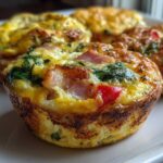 Close-up of freshly baked Egg Muffin Cups filled with ham, spinach, and red pepper on a white plate.