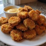 A pile of crispy, golden brown Fried Pickles served on a white plate next to a small ramekin of yellow dipping sauce.