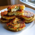 A stack of perfectly pan-fried mashed potato cakes, showing a fluffy interior with chives, ready to eat.