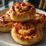 A close-up stack of four golden brown, cheesy pizza pinwheels topped with mini pepperoni slices.