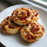 Close-up of four freshly baked pizza pinwheels stacked on a white plate, showing melted cheese and pepperoni.