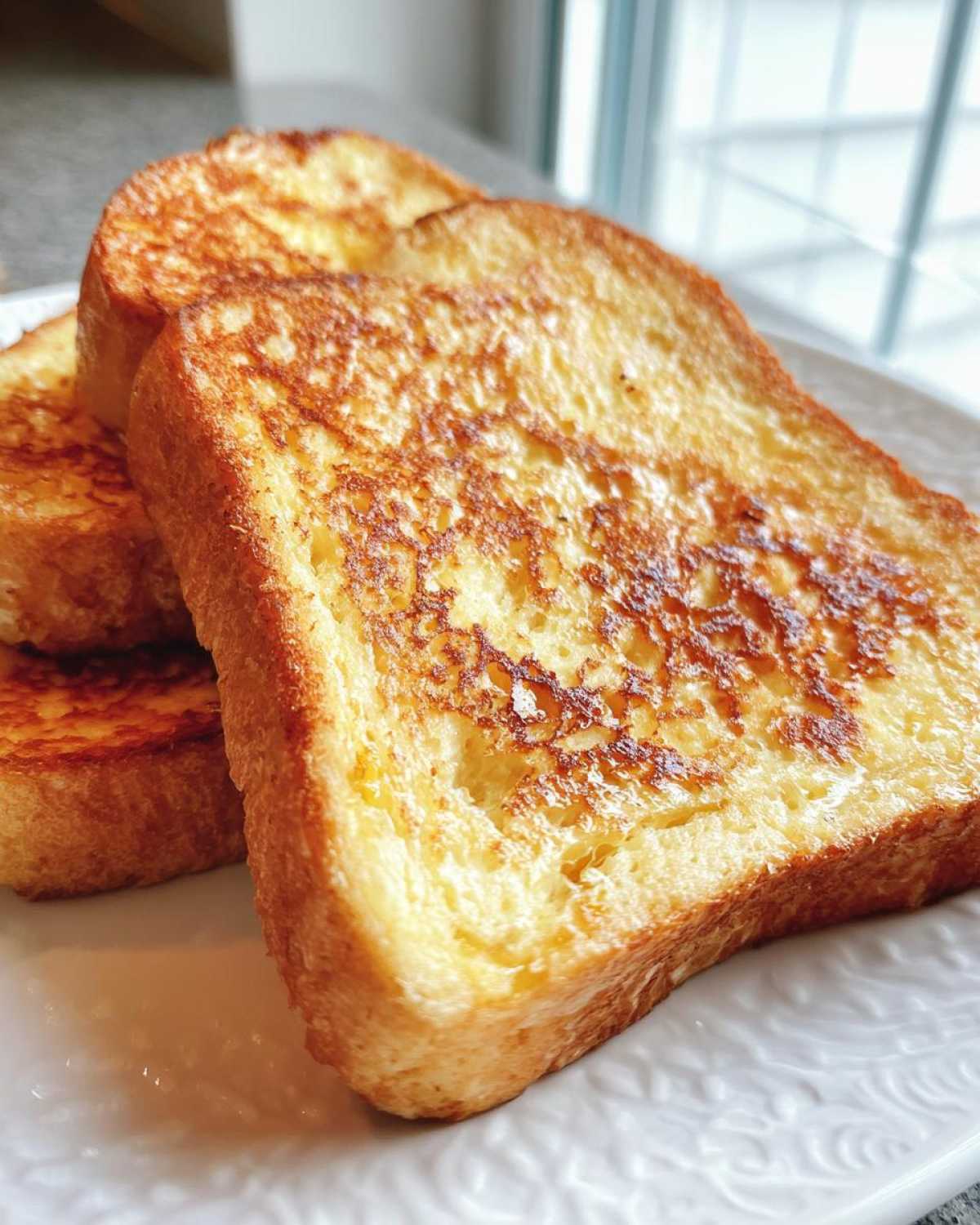 Close-up of three golden-brown slices of protein french toast stacked on a white plate.