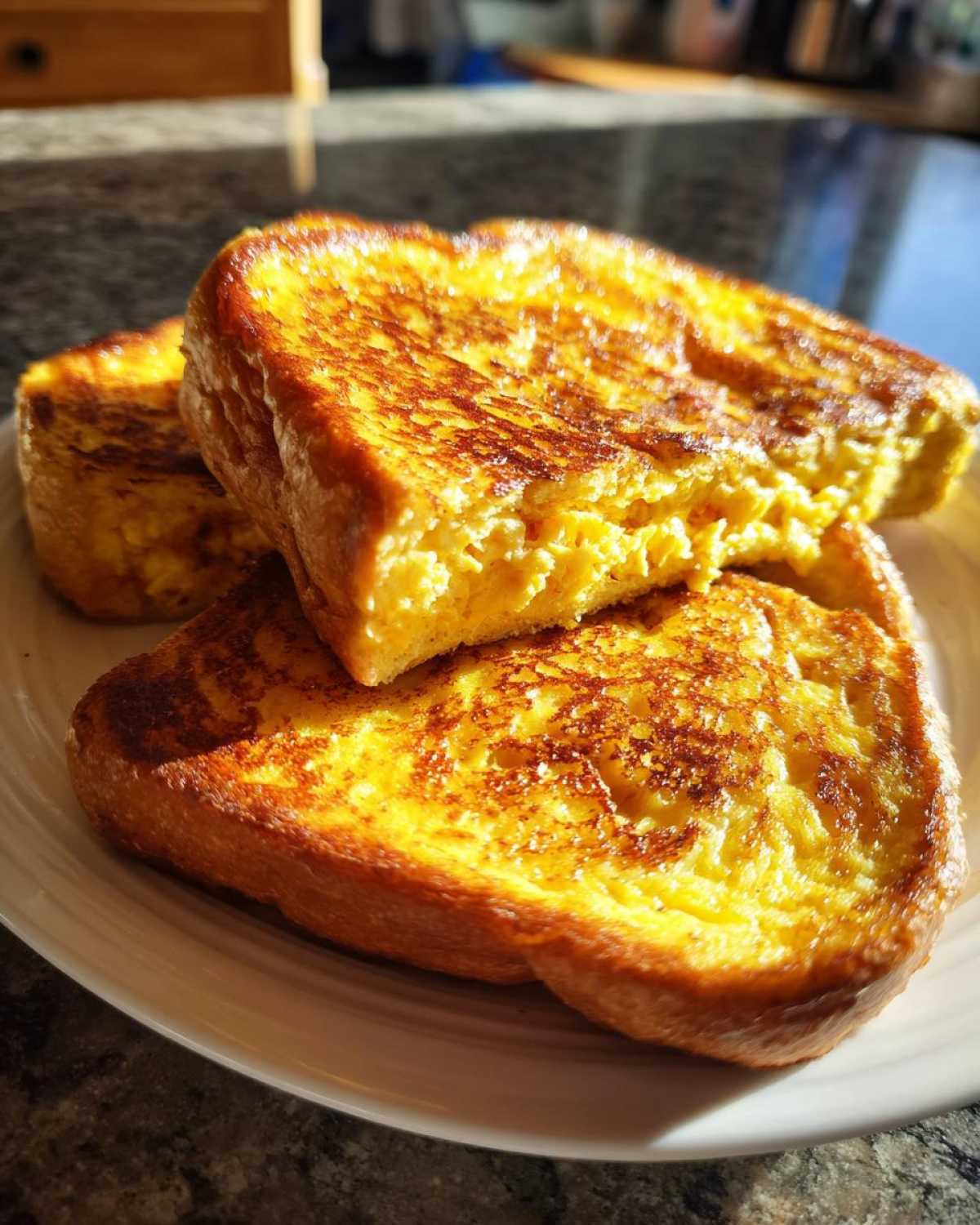 Close-up of three thick slices of golden brown protein french toast stacked on a white plate.