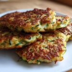 A stack of four golden brown, pan-fried zucchini fritters showing shredded green zucchini inside.