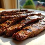 Close-up of perfectly grilled and sliced steak coated in a flavorful carne asada marinade, resting on a white plate.