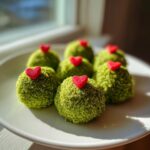 Plate of bright green grinch oreo balls, each topped with a small red heart candy.