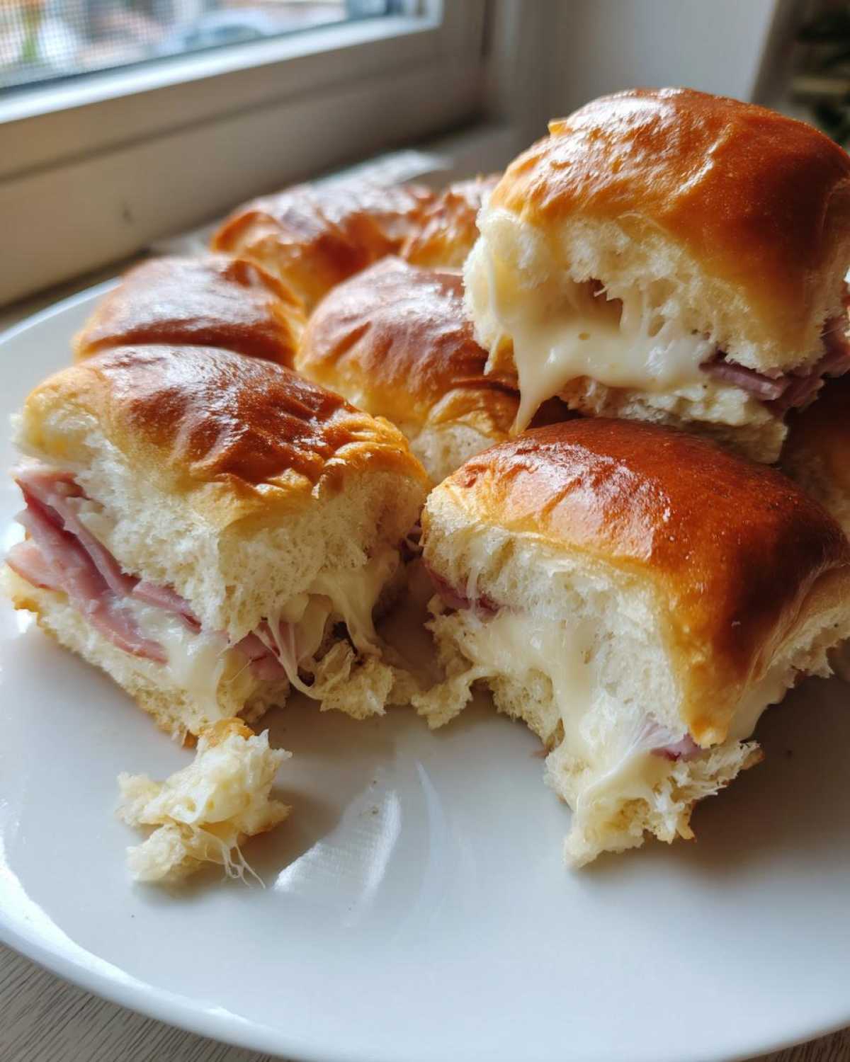 Close-up of freshly baked Ham and Cheese Sliders with gooey, melted cheese stretching out.