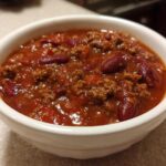 Close-up of a white bowl filled with rich, thick crockpot chili featuring ground beef and kidney beans.