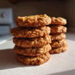 A tall stack of golden brown oatmeal breakfast cookie rounds catching the morning light.