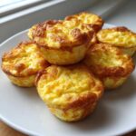 A stack of fluffy, golden brown, high-protein egg bites served on a white plate near a window.