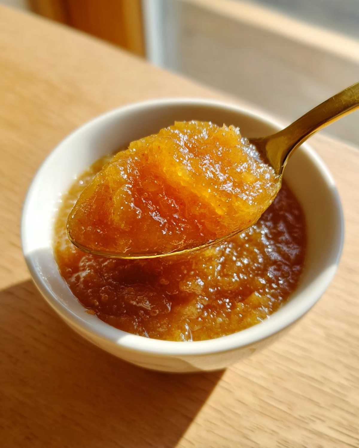 A golden spoon lifting a spoonful of chunky, homemade applesauce from a white bowl.