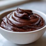 Close-up of rich, dark homemade chocolate pudding swirled high in a small white bowl.