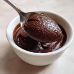 A spoonful of thick, rich homemade chocolate pudding being lifted from a white bowl.