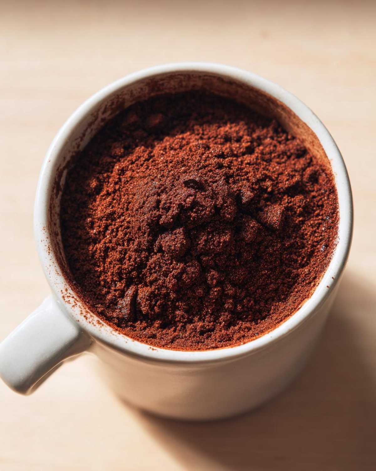 Overhead close-up of rich, dark brown hot cocoa mix powder filling a white ceramic mug.