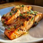 Close-up of two perfectly cooked, juicy air fryer salmon fillets topped with melted butter and fresh parsley.