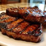Close-up of three perfectly grilled and glazed pork steak cuts resting on a white plate.