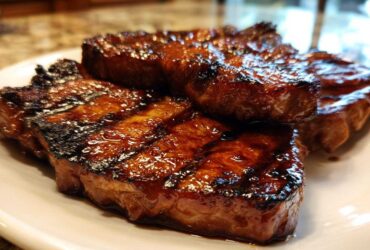 Close-up of three perfectly grilled and glazed pork steak cuts resting on a white plate.