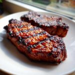 Two perfectly grilled, glazed pork steak pieces with visible grill marks on a white plate.