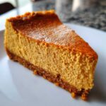 Close-up of a rich, orange slice of keto pumpkin cheesecake on a white plate.