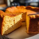 A thick slice of baked keto pumpkin cheesecake showing its dense texture, next to the rest of the cake.