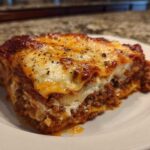 A thick, cheesy slice of lasagna with cottage cheese and meat sauce on a white plate.