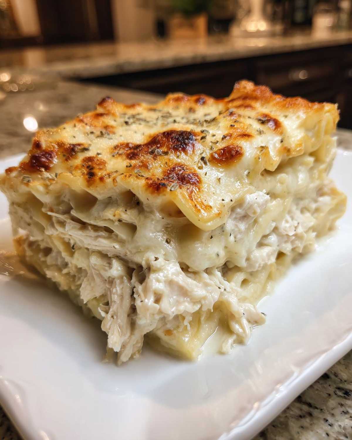 A close-up of a thick, layered slice of white chicken lasagna topped with browned, bubbly cheese.