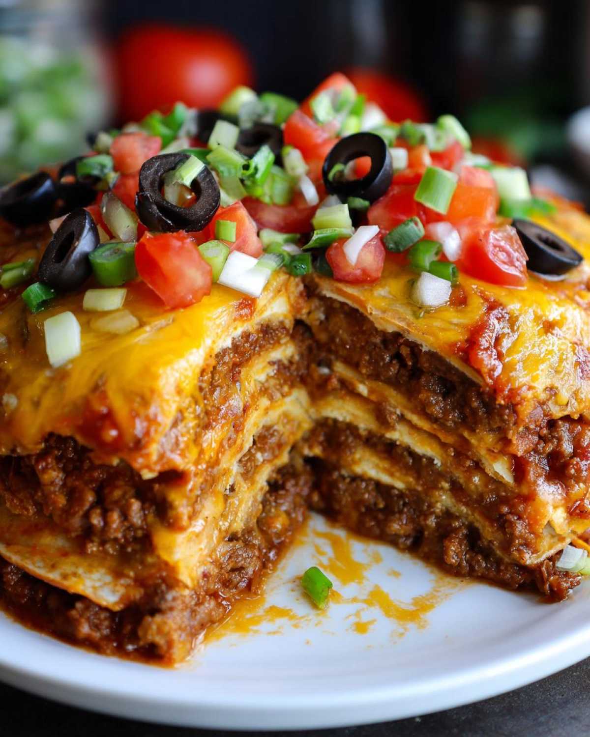 Cross-section view of a layered Mexican pizza filled with seasoned ground beef and topped with melted cheese, tomatoes, olives, and green onions.