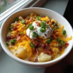 A close-up of a bowl of loaded baked potato soup topped with sour cream, shredded cheddar, bacon bits, and green onions.