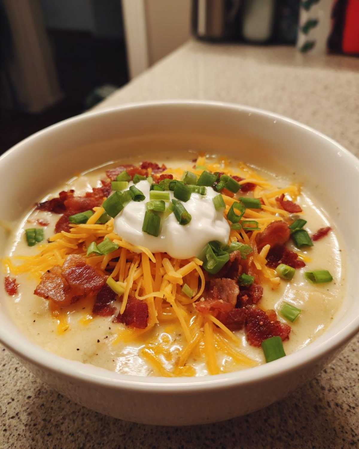 A hearty bowl of loaded baked potato soup topped with shredded cheddar, bacon bits, sour cream, and chives.