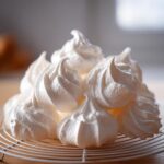 A close-up pile of perfectly piped white meringue cookies resting on a wire cooling rack.