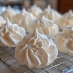 Close-up of perfectly piped white meringue cookies cooling on a wire rack.