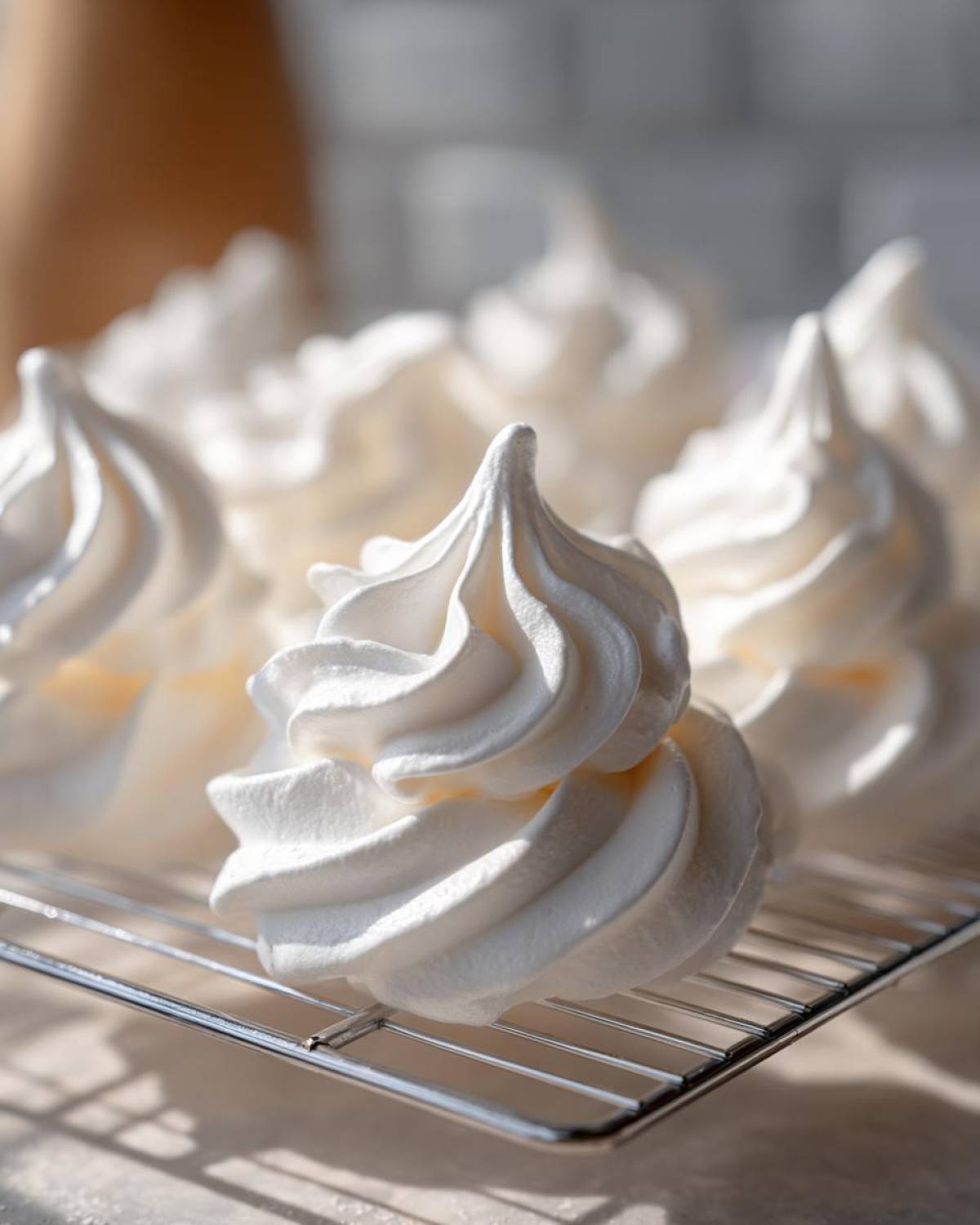 Close-up of crisp, white meringue cookies with defined swirls cooling on a wire rack.