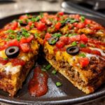 A close-up view of a thick-crust Mexican pizza, topped with seasoned beef, melted cheese, salsa, black olives, and green onions.