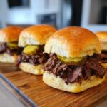 Close-up of Mississippi pot roast sliders piled high with shredded beef and pickles on soft buns.