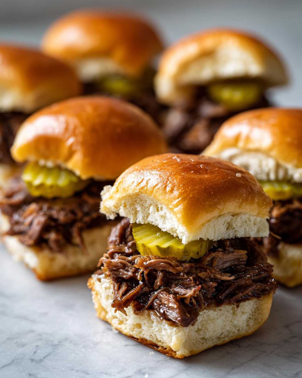 Close-up of several Mississippi pot roast sliders piled high with shredded beef and pickles on soft buns.
