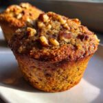 Close-up of a moist banana nut muffin topped generously with chopped pecans, golden brown from baking.