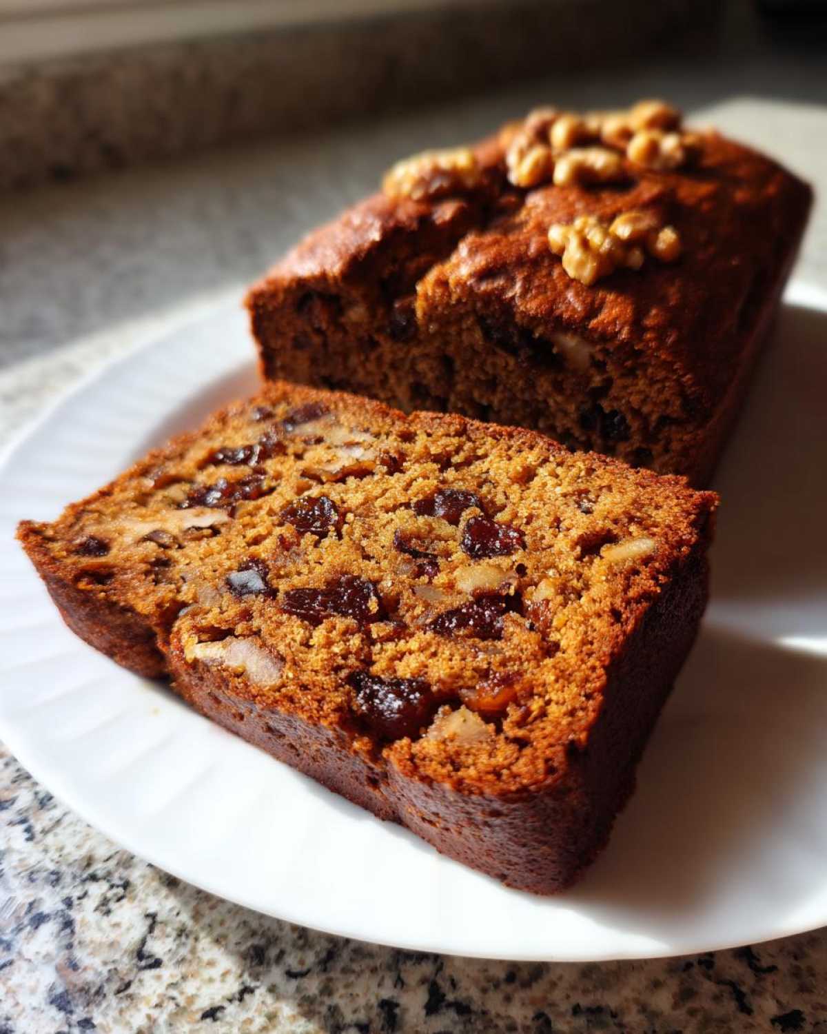 A close-up of a moist slice of date nut bread, showing dark raisins and walnuts embedded in the rich brown crumb.