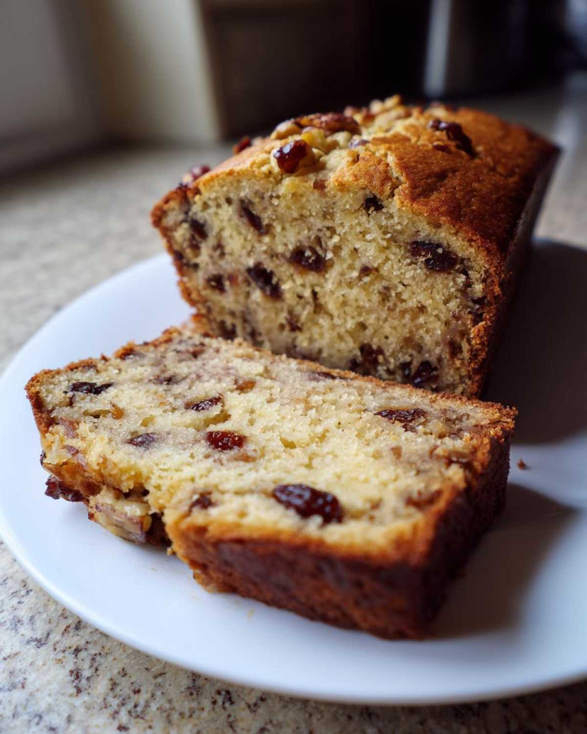 A moist slice of date nut bread is cut from the loaf, showing raisins and nuts throughout the crumb.
