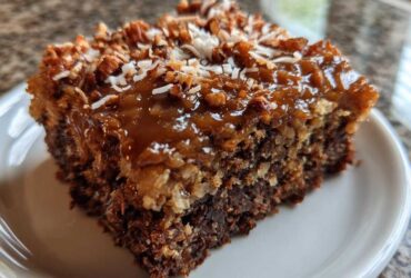 Close-up of a moist slice of german chocolate poke cake topped with gooey caramel, pecans, and coconut.